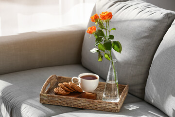 Vase with beautiful roses and cup of coffee on sofa in room