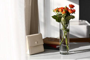 Vase with bouquet of beautiful roses and bag on table in room
