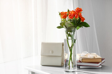 Vase with bouquet of beautiful roses and bag on table in room