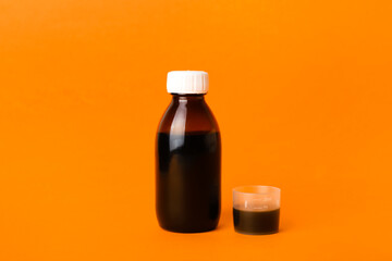 Bottle of cough syrup and cup on orange background