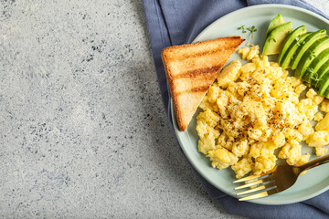 Plate with tasty scrambled eggs, avocado and toast on light background