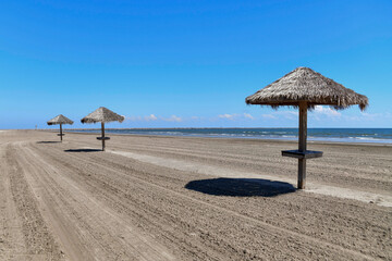 palapas on a deserted, empty beach with surf and a jetty in the distance