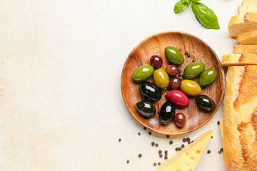 Plate of tasty olives and bread on light background