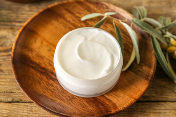 Plate with jar of natural olive cream on wooden table, closeup