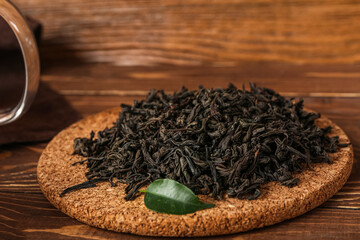Board with heap of dry puer tea on wooden background, closeup