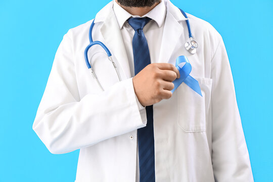 Male urologist with blue awareness ribbon on color background. Prostate cancer concept