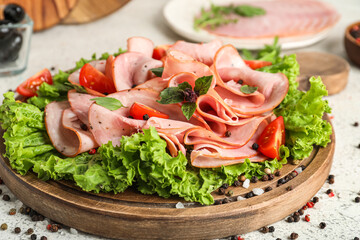 Wooden board with sliced ham, lettuce and spices on light table, closeup