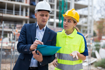 Civil engineer and a young woman worker working on a construction site discuss a construction plan,...
