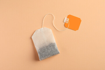New tea bag with tab on pale orange background, top view