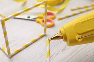 Making craft with hot glue gun and straws on white wooden table, closeup