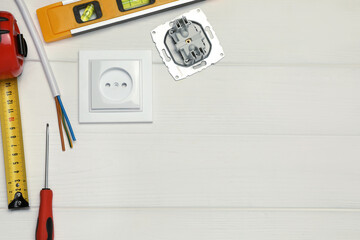 Power socket and set of electrician's tools on white wooden table, flat lay. Space for text