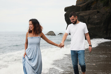 Happy young couple walking on beach near sea