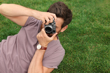 Man with camera taking photo on green grass, space for text. Interesting hobby