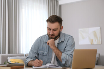Naklejka premium Young man taking notes during online webinar at table indoors