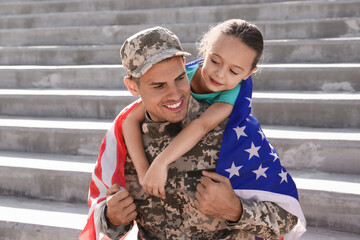 Soldier with flag of USA and his little daughter outdoors
