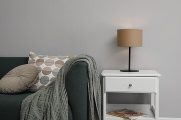 Stylish lamp on bedside table near sofa in room