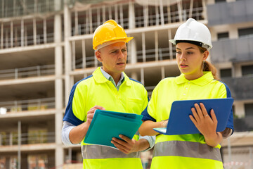 Man and woman builders in uniform and hardhats discussing while standing in construction site....