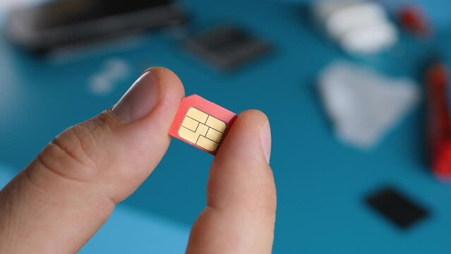 Mans hand hold red micro SIM card in repair service office. Disassembled smartphone blue background. Communication equipment at laboratory. 5g network or travel sim card concept. Chip and connections