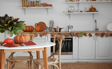 Vase with leaves and fresh pumpkins on dining table in light kitchen