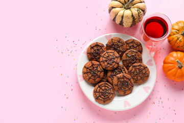 Plate with Halloween spiderweb cookies, pumpkins and glass cup of tea on pink background