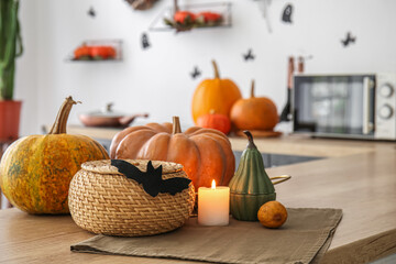 Halloween pumpkins with basket and burning candle on counter in kitchen