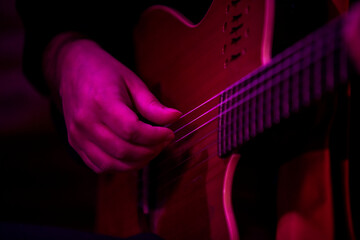Hand of a musician playing the taut strings of a guitar bathed in rgb light