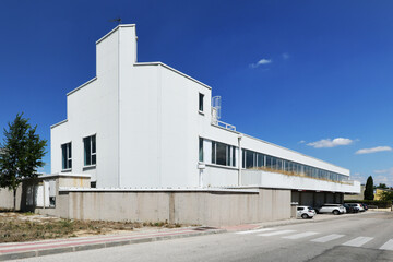 Facade of a lonely industrial building with white cladding, many windows and a clear blue sky