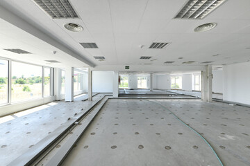 Empty industrial building with concrete floors, awaiting new coverage with large windows and white technical ceiling
