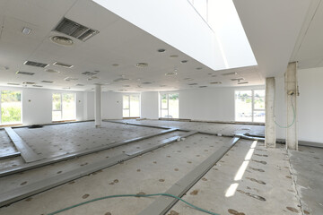 Empty industrial warehouse with concrete floors, waiting for new coverage with large windows and white technical ceiling and metal gutters