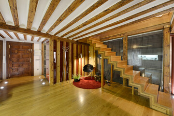 Living room with wooden staircase in a duplex house with wooden paneled front door