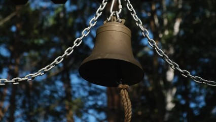 Big copper and bronze bell hanging on chains outdoor. Ringing metal bell close up.