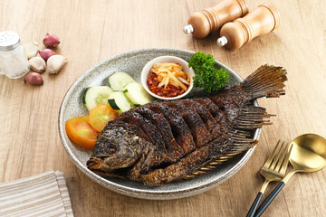 Gurame Bakar Madu, Grilled Gourami with honey and soy sauce. Served with sambal (chilli sauce), cucumber and tomatoes in white plate.   
