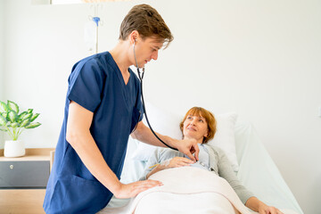 Fototapeta premium Young Caucasian doctor use stethoscope to check or diagnosis the symptom of senior patient who lie on bed in patient room.