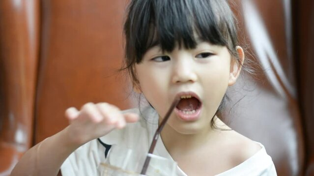 Little asian girl Sucking sweet tea lemon from a plastic straw happily in the coffee shop. closeup face