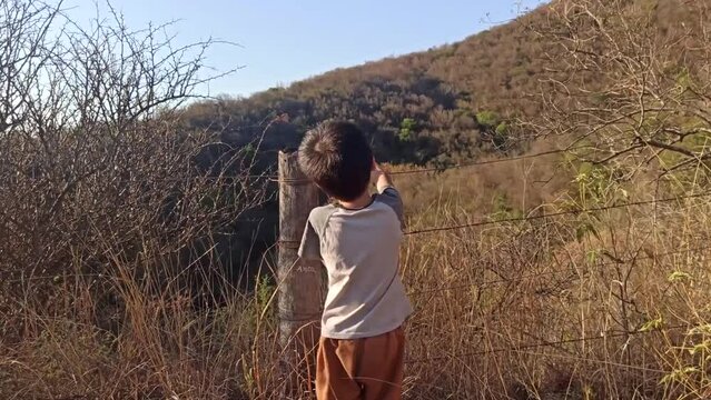 ni&ntilde;o se&ntilde;alando los cerros parado junto a un alambrado