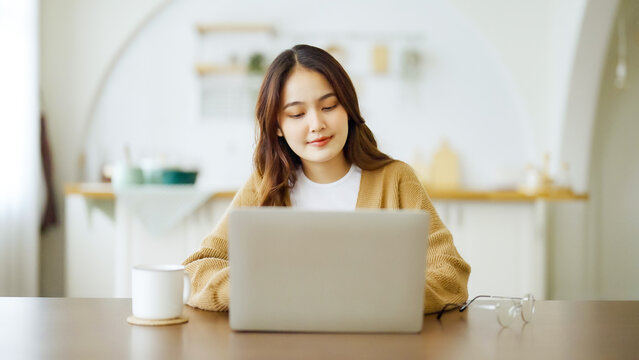 Smiling Asian Young Woman Working On Laptop At Home Office. Young Asian Student Using Computer Remote Studying, Virtual Training, E-learning, Watching Online Education Webinar At House