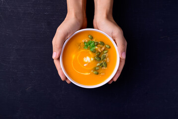 Butternut squash pumpkin soup in bowl holding by hand on black background, Homemade food in autumn...