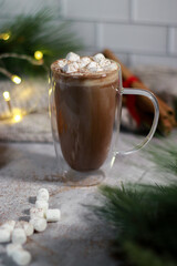 hot chocolate in a glass mug with mini marshmallows on grey table, blurred xmas background 
