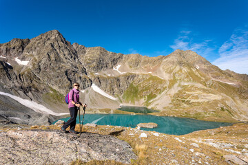 Naklejka premium The girl stands against the backdrop of mountain peaks and a blue lake. Beautiful mountain landscape for vacation, travel and healthy lifestyle