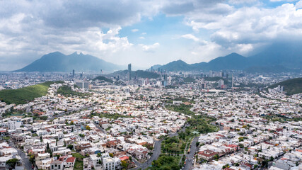 Obraz premium Drone photo of Monterrey city skyline with blue sky and clouds, famous Cerro de la Silla mountain in the background.