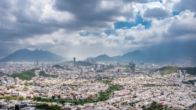 Aerial photograph of Monterrey, Nuevo León Mexico, set against a vivid blue sky with clouds. Prominently featured in the background is the iconic Cerro de la Silla mountain