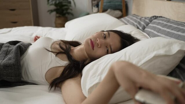 closeup view of an asian female waking to the alarm triggered on her phone is turning it off and checking time in the morning on bed in the bedroom at home.
