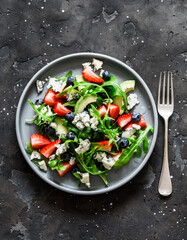 Fototapeta na wymiar Arugula, strawberry, gorgonzola, avocado salad on a dark background, top view