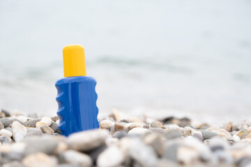 Sunblock in a bottle. Lotion in a blue and yellow package against a background of pebbles and the sea. Mockup.