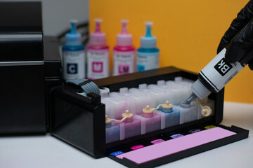 Employees refilling ink into a ink tank printer at home office. Hand holding blue ink cartridge and...