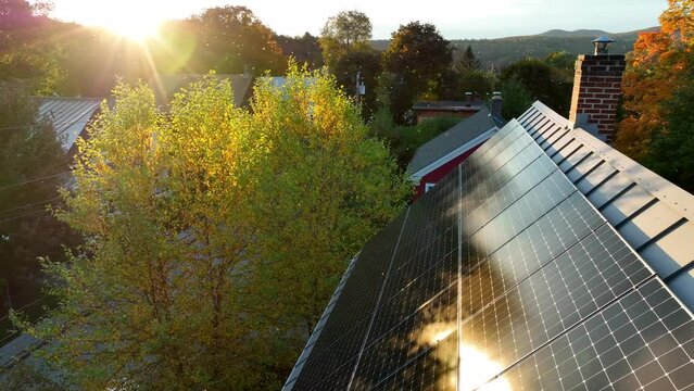 Rooftop solar panel array. Green clean renewable energy theme. Beautiful sunlight reflects to generate electricity. Aerial in autumn, colorful foliage.