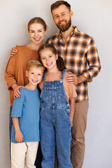 Happy family mother father and children standing against empty grey wall