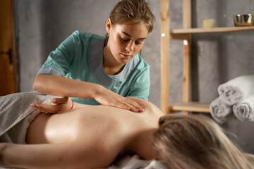 masseur massaging shoulder of young woman. Female patient getting remedial body and shoulder blade...