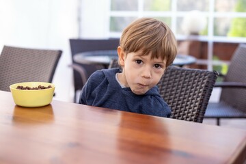 Little boy sit on chair at table in empty hall in cafe and staring chew food. Alone kid of...