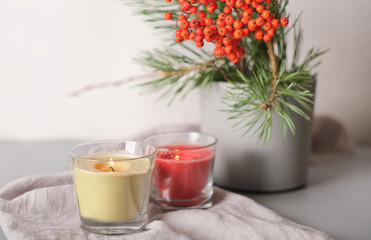 rowanberry and pine branch in a concrete vase and glowing candles on grey background. blog autumn content. thanksgiving home decor